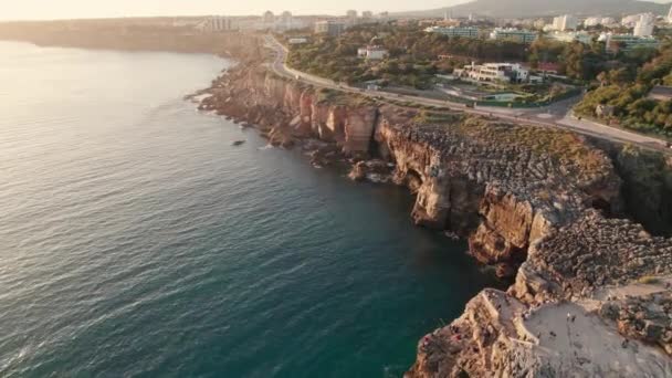 Pemandangan udara pantai berbatu oleh laut di kota Cascais saat matahari terbenam, Portugal — Stok Video