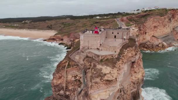 Luchtfoto van een vuurtoren op een klif met een fort in Nazare, Portugal — Stockvideo