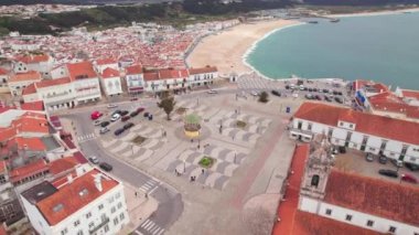 Portekiz 'in güzel sahil kasabası Nazare üzerinde uçuyor. Tarihsel kasaba meydanı, kilise ve genişleyen beyaz Nazare kumsal plajı, sahil beldesi, Portekiz. Panoramik hava görüntüsü