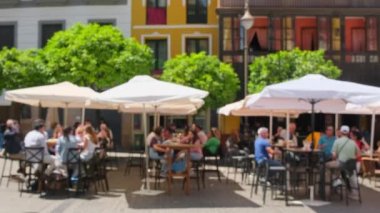 Geleneksel Avrupa açık hava kafesinin odaklı olmayan görüntüsü. İnsanlar güneşli bir yaz gününde Avrupa 'nın bilinmeyen bir şehrinde bir açık hava restoranında içiyor, yiyor ve sohbet ediyorlar. Bulanık gerçek zaman sahnesi