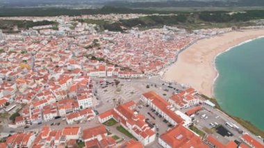 Portekiz 'in güzel sahil kasabası Nazare üzerinde uçuyor. Tarihsel kasaba meydanı, kilise ve genişleyen beyaz Nazare kumsal plajı, sahil beldesi, Portekiz. Panoramik hava görüntüsü