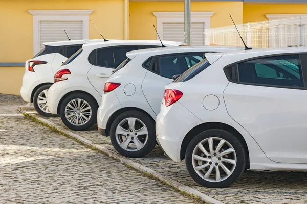 Four similar white hatchback cars but from different car manufacturers parked on the cobbled street in typical European town. Budget car rental and retail concept