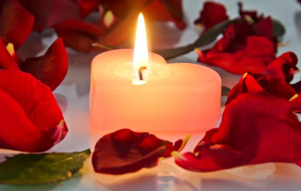 Hořící svíčka v růžových lístků — Stock fotografie