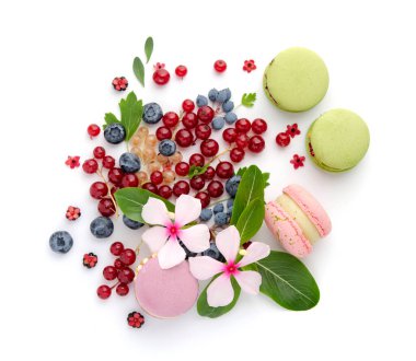 Kırmızı ve mavi böğürtlen serpintisi. Beyaz çiçekler ve yeşil yapraklar. Çok renkli badem kurabiyeleri.