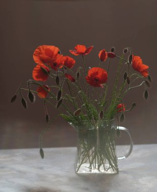 Bir buket çiçek. Kırmızı gelincikler yabani çiçeklerdir. Cam çaydanlık..