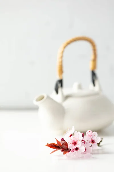 Λευκή κεραμική τσαγιέρα και ανοιξιάτικα λουλούδια σε λευκό τραπέζι, επιλεκτική εστίαση — Φωτογραφία Αρχείου