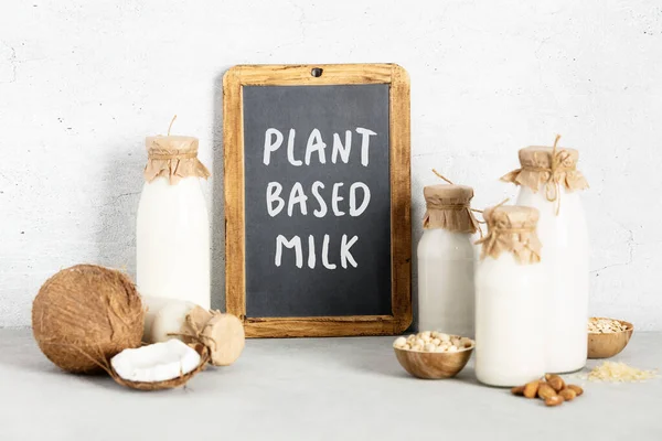 Melk op basis van niet-zuivelgewassen in flessen, ingrediënten en schoolbord met plantaardige melkbelettering op lichte ondergrond — Stockfoto