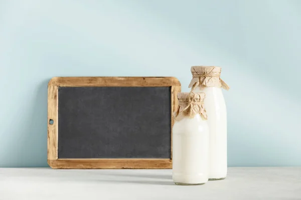 Milch in Flaschen und Kreide auf hellblauem Hintergrund — Stockfoto