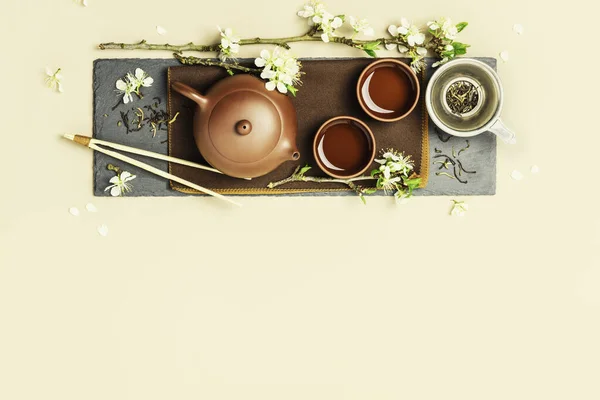 Conjunto de té asiático en pizarra de piedra, tetera de cerámica, tazas, té seco y ramas de primavera — Foto de Stock