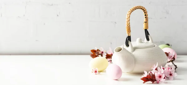 Paskalya kompozisyonu beyaz seramik çaydanlık, Paskalya yumurtaları ve bahar çiçekleri beyaz masa üzerinde, boşluğu kopyala — Stok fotoğraf