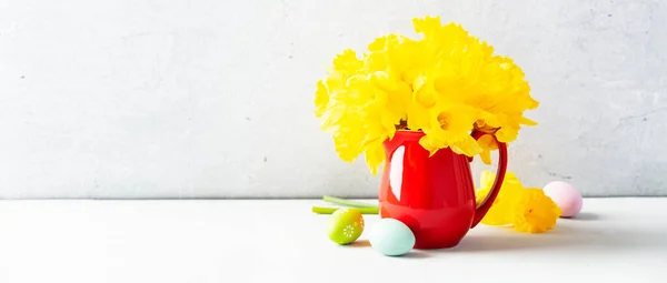 Paskalya yumurtaları ve sarı nergis buketi masanın üstünde kırmızı bir sürahi, Paskalya kompozisyonu, ev dekorasyonu, iç dekorasyon. — Stok fotoğraf