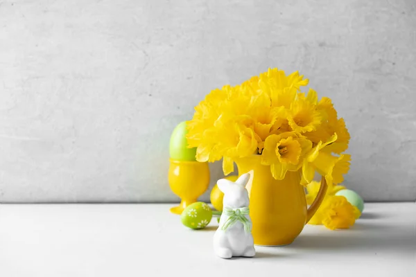Huevos de Pascua, conejito y ramo de narcisos amarillos en una jarra amarilla en la mesa, composición de Pascua, decoración del hogar, interior, — Foto de Stock