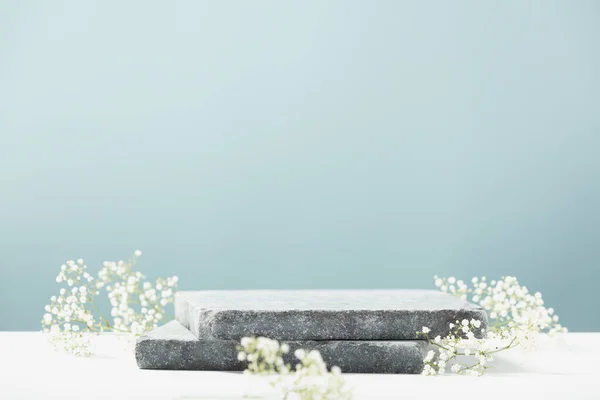 Pedestal de granito plano y flores blancas sobre fondo azul. Escaparate para productos cosméticos. Anuncio de productos. Diseño de estilo de diseño. — Foto de Stock