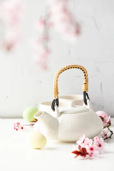 Easter composition with White ceramic teapot, Easter eggs and spring flowers on white table, selective focus — Stock Photo, Image
