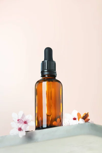 Amber glass dropper bottle and spring cherry blossom flower on marble shelf. Skincare products , natural cosmetic. Beauty concept for face and body care, ow angle view, — Foto Stock