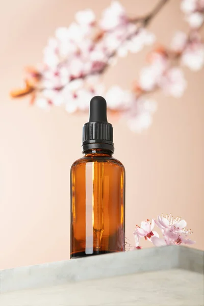 Amber glass dropper bottle and spring cherry blossom flower on marble shelf. Skincare products , natural cosmetic. Beauty concept for face and body care, ow angle view, — Stock Photo, Image