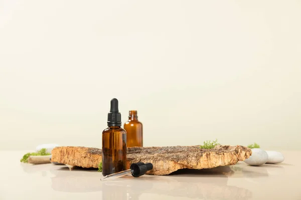 Trendy composition of Blank amber glass essential oil bottles, bark tree and moss on beige background. Product, cosmetic, perfume, jewellery mock up — Stock Photo, Image