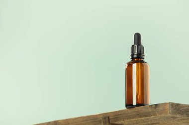 Ahşap rafta siyah kapaklı kehribar cam damlası şişesi, yeşil arka plan. SPA doğal organik güzellik ürünü ambalaj tasarımı, markalaşma. Güzellik salonu modeli, düşük açılı, göz hizasının altında.