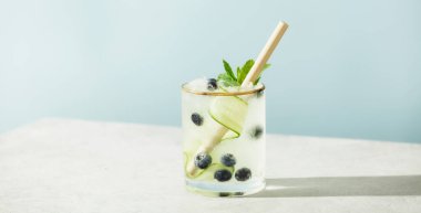 Trendy summer drinks with cucumber, mint and blueberry on blue sky background. Vacation concept clipart