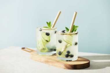 Trendy summer drinks with cucumber, mint and blueberry on blue sky background clipart