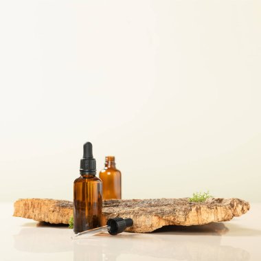 Boş kehribar camının modaya uygun bileşimi esaslı yağ şişeleri, ağaç kabuğu ve bej arka planda yosun. Organik kozmetik ürünler için soyut podyum. Kopyalama alanı olan en küçük konsept.