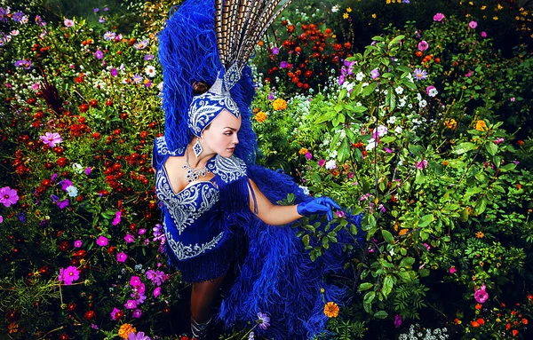 Vrouw in dure exotische carnaval pak pose in weide van bloemen. — Stockfoto