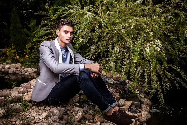 Portrait of young beautiful fashionable man against autumn garden. — Stock Photo, Image