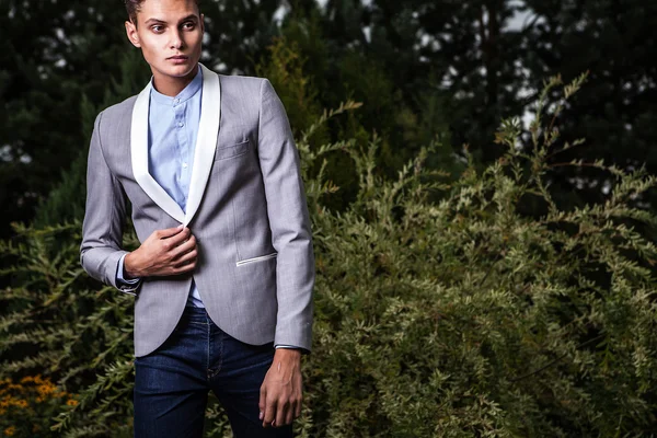 Portrait of young beautiful fashionable man against autumn garden. — Stock Photo, Image