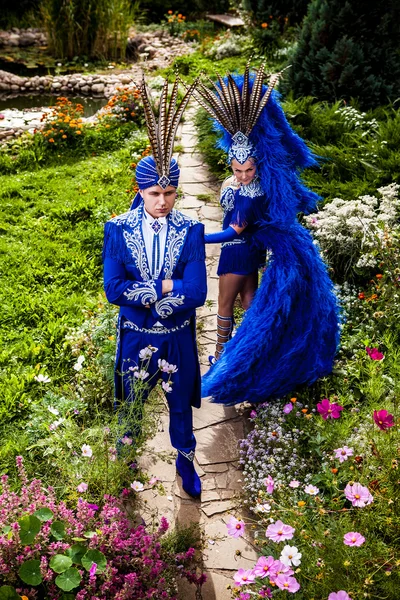 Couple in expensive dark blue costume of illusionist pose in fairy tale flowers park. — Stock Photo, Image