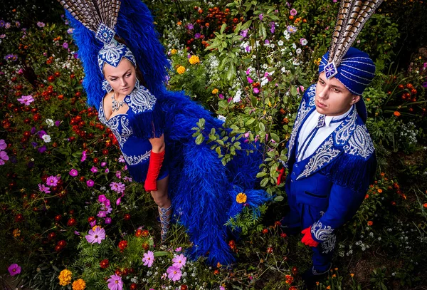 Couple in expensive dark blue costume of illusionist pose in fairy tale flowers park. — Stock Photo, Image