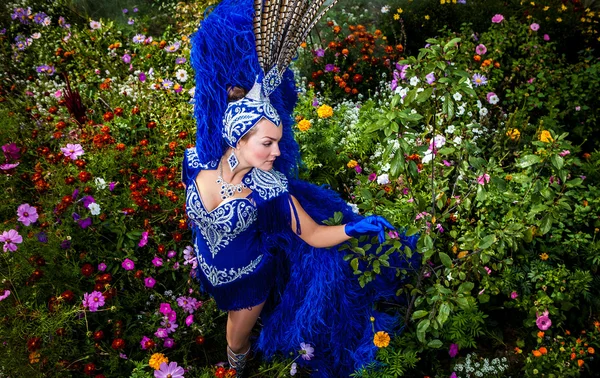 Vrouw in dure exotische carnaval pak pose in weide van bloemen. — Stockfoto