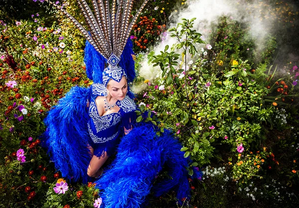 Kvinna i dyra exotiska karneval kostym pose på äng med blommor. — Stockfoto