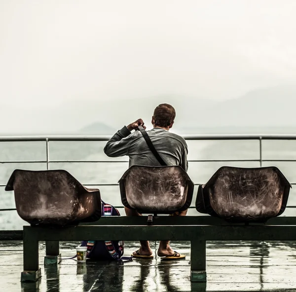 Mann sitzt am Pier und blickt aufs Meer — Stockfoto