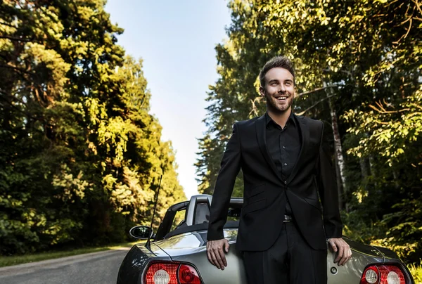 Elegante joven feliz hombre en coche descapotable al aire libre . — Foto de Stock