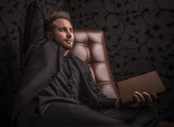 Handsome young man in dark suit relaxing on luxury sofa. — Stock Photo, Image