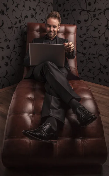 Όμορφος νεαρός άνδρας στο χαλαρωτικό στον καναπέ πολυτελές σκούρο κοστούμι. — Φωτογραφία Αρχείου