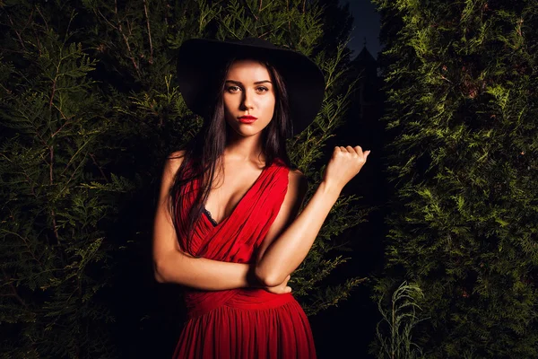 Beleza morena mulheres em vestido vermelho & chapéu posar no parque noturno . — Fotografia de Stock