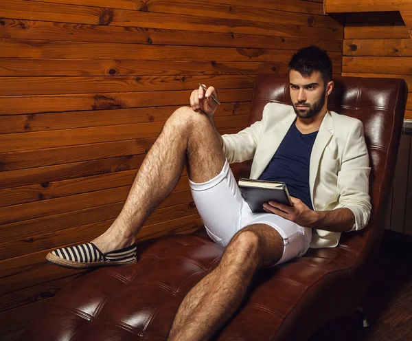 Handsome young man in white suit relaxing on luxury sofa with diary. — Stock Photo, Image