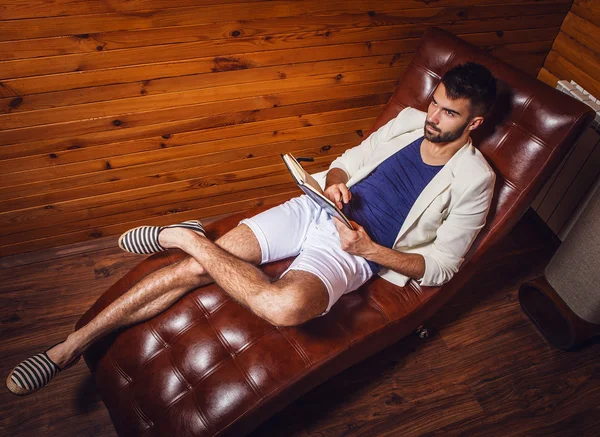 Όμορφος νεαρός άνδρας με λευκό κοστούμι χαλαρωτικό στον καναπέ πολυτέλεια με το ημερολόγιο. — Φωτογραφία Αρχείου