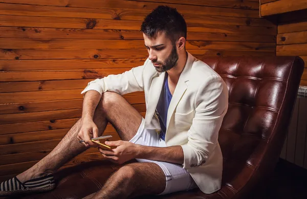 Красивый молодой человек в белом костюме расслабляется на роскошном диване с дневником . — стоковое фото