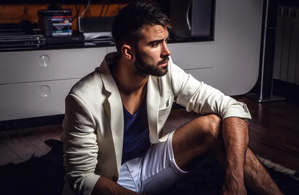 Jeune homme barbu attrayant en costume blanc pose dans la chambre moderne . — Photo