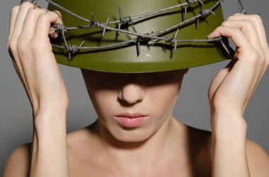 Жінка тримає військових шолом руки з колючого дроту