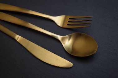 Gold knife, fork and spoon on a black stone background - Food concept photography