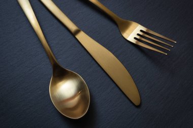Gold knife, fork and spoon on a black stone background - Food concept photography