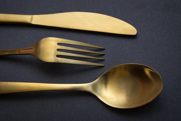 Gold knife, fork and spoon on a black stone background - Food concept photography