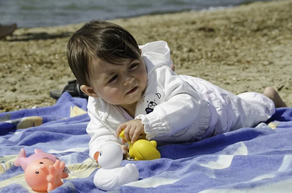 Bebê menina relaxante e jogando em uma toalha de praia — Fotografia de Stock