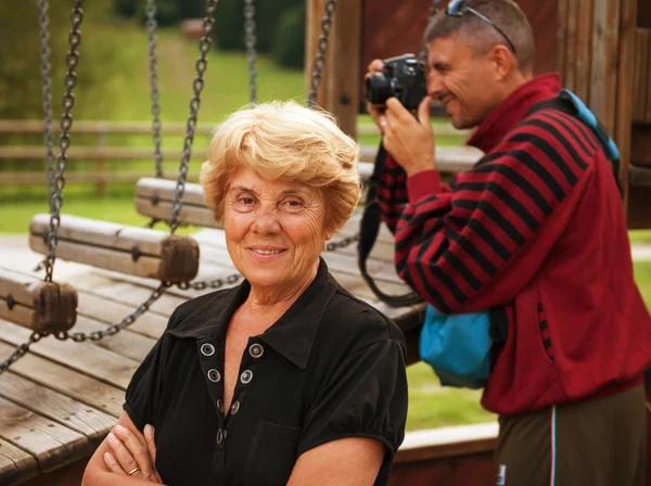 Senior vrouw in het park met fotograaf op achtergrond — Stockfoto