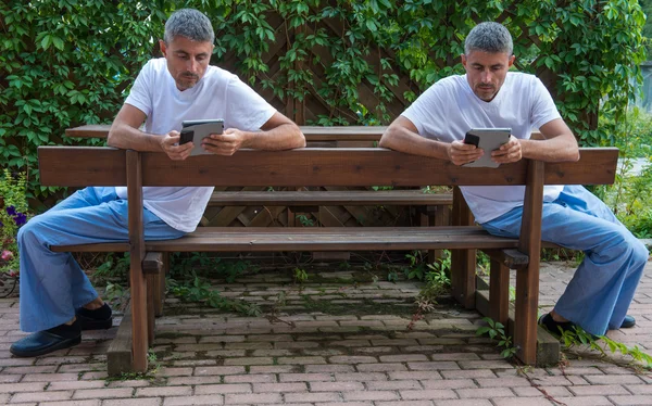 Twins on the bench reading tablet outdoor — Stock Photo, Image