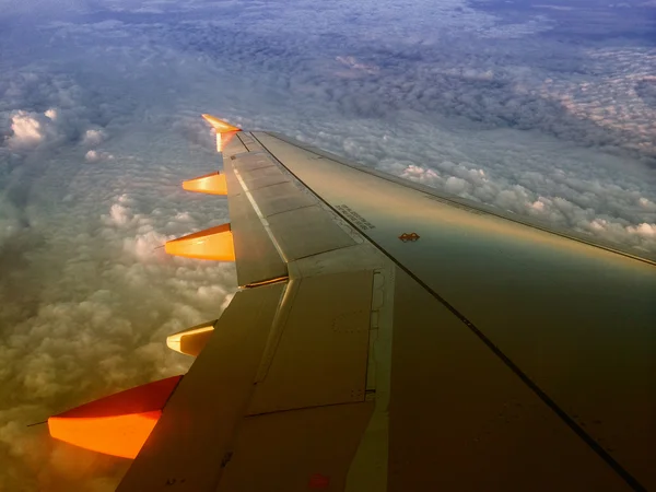 Wing of an airplane flying above the clouds at sunset — Stock Photo, Image