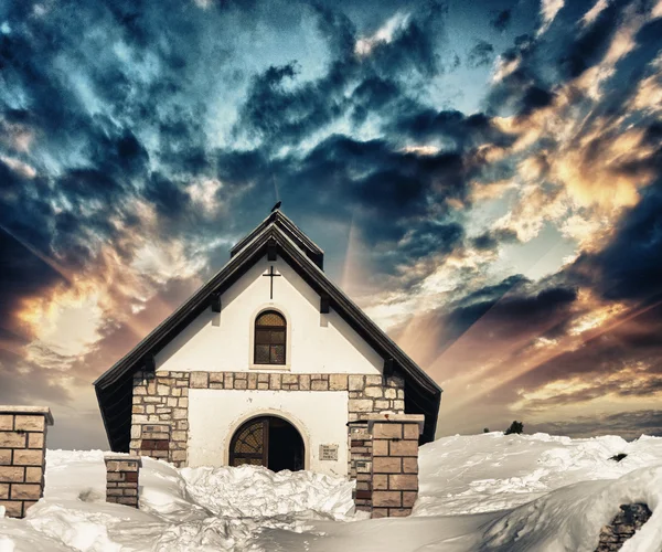 Kleine Kirche auf einem verschneiten Berggipfel. schöner Wintersonnenuntergang c — Stockfoto